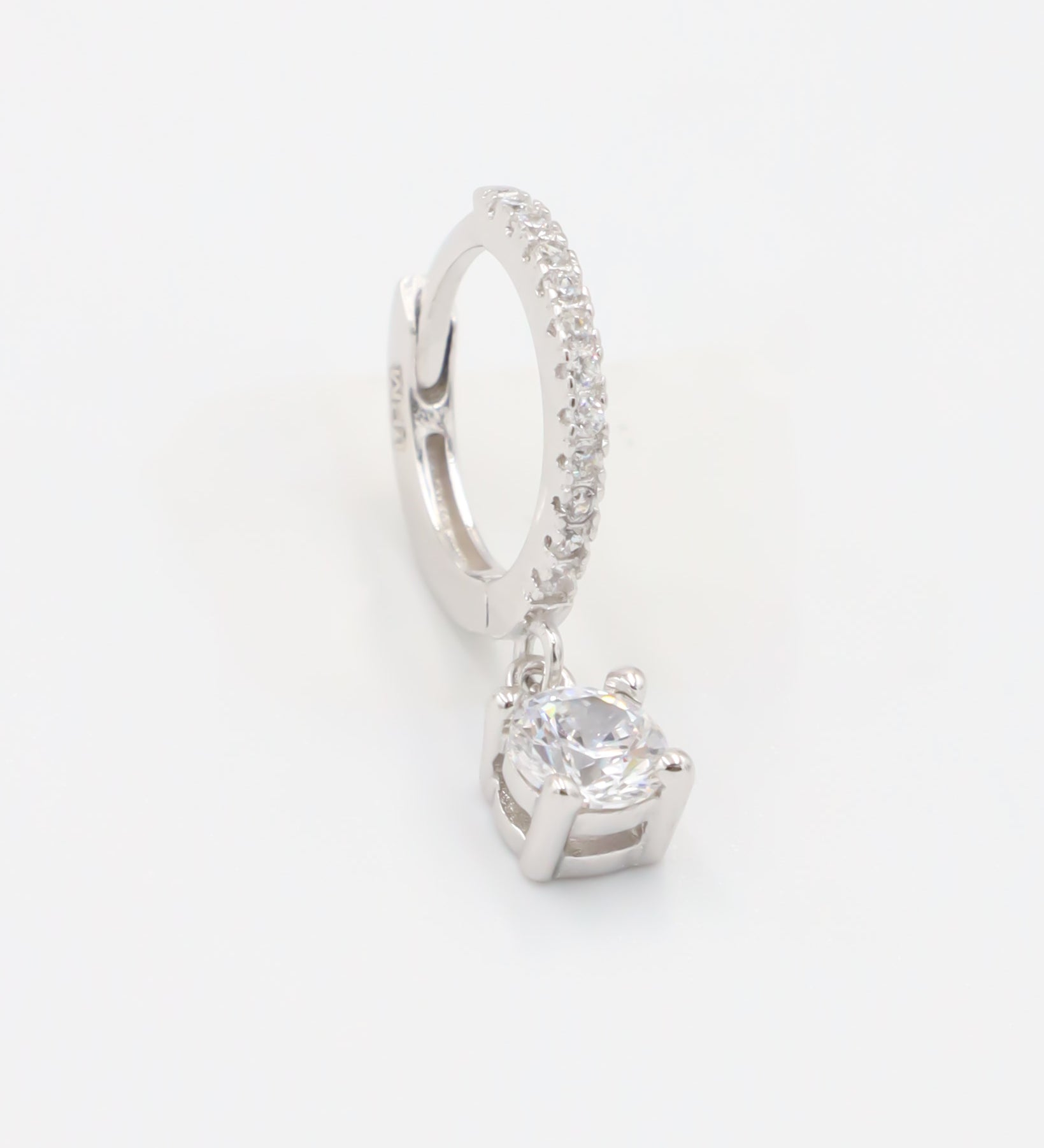 A silver hoop earring with a hinged clasp and a central gemstone, possibly a diamond, surrounded by smaller stones.