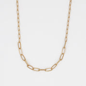 A gold-colored necklace with a chain link pattern laid out on a plain surface.