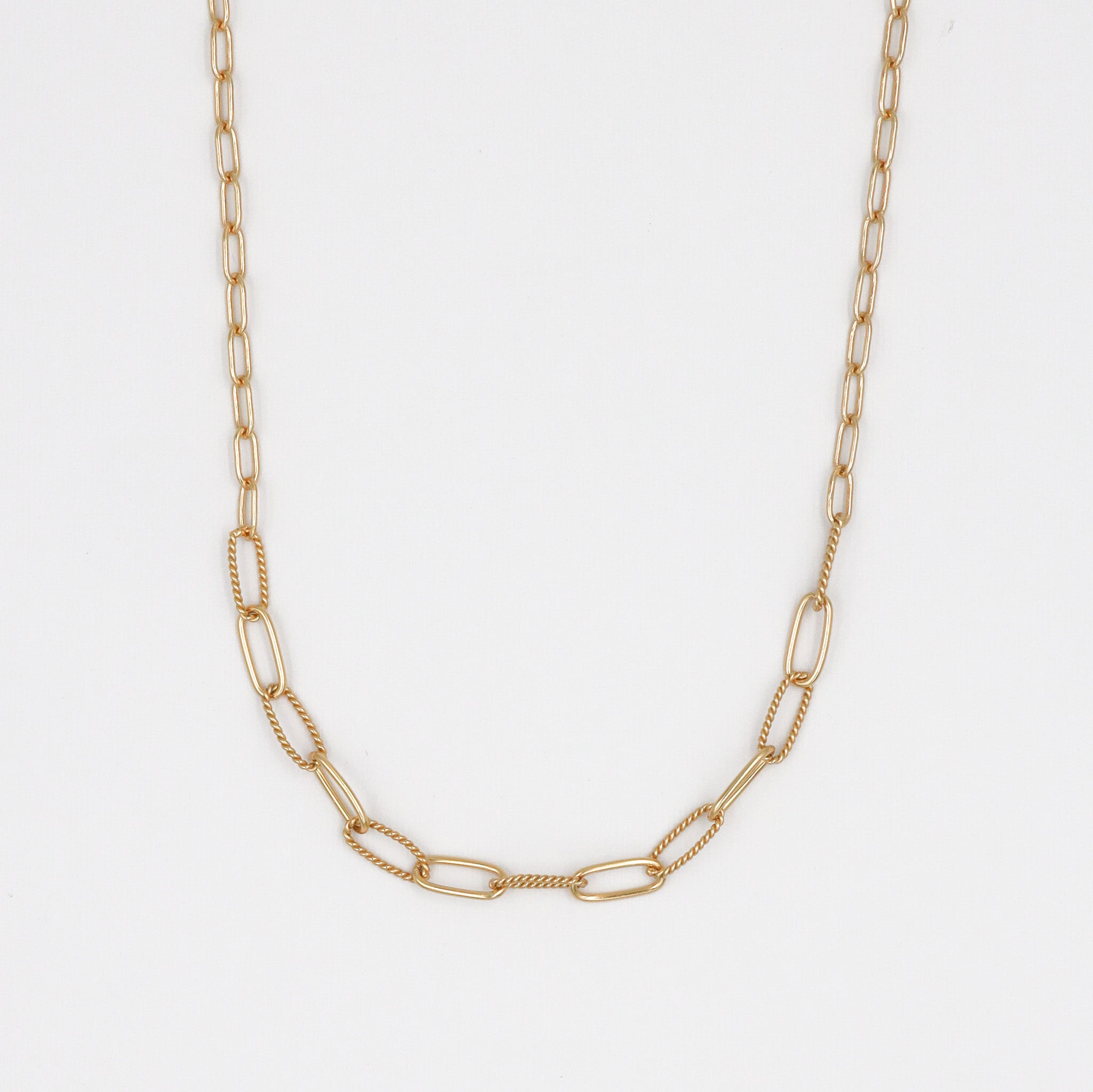 A gold-colored necklace with a chain link pattern laid out on a plain surface.
