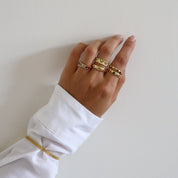 A gold-colored ring with multicolored gemstone accents worn on a hand and combined with other rings. 