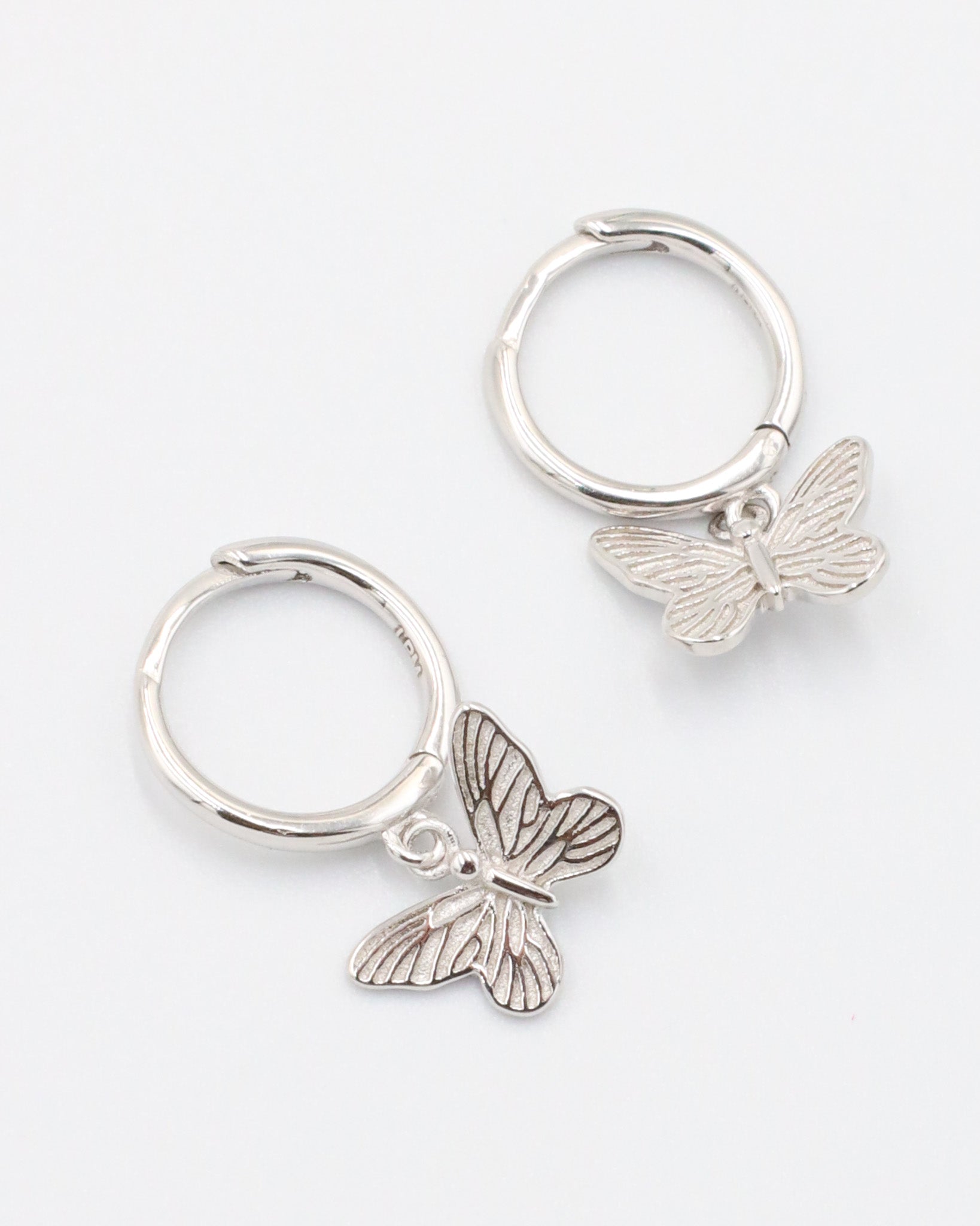 A silver hoop earring with a butterfly charm attached to it, displayed on a white background.