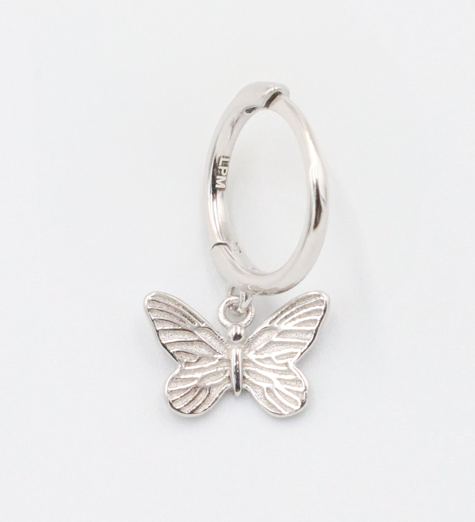 A silver hoop earring with a butterfly charm attached to it, displayed on a white background.