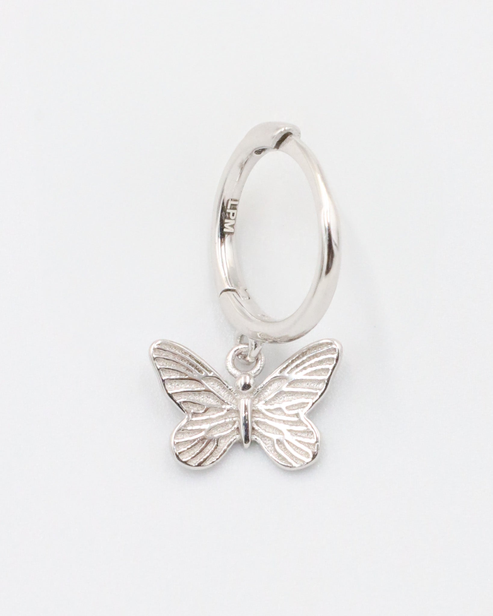A silver hoop earring with a butterfly charm attached to it, displayed on a white background.