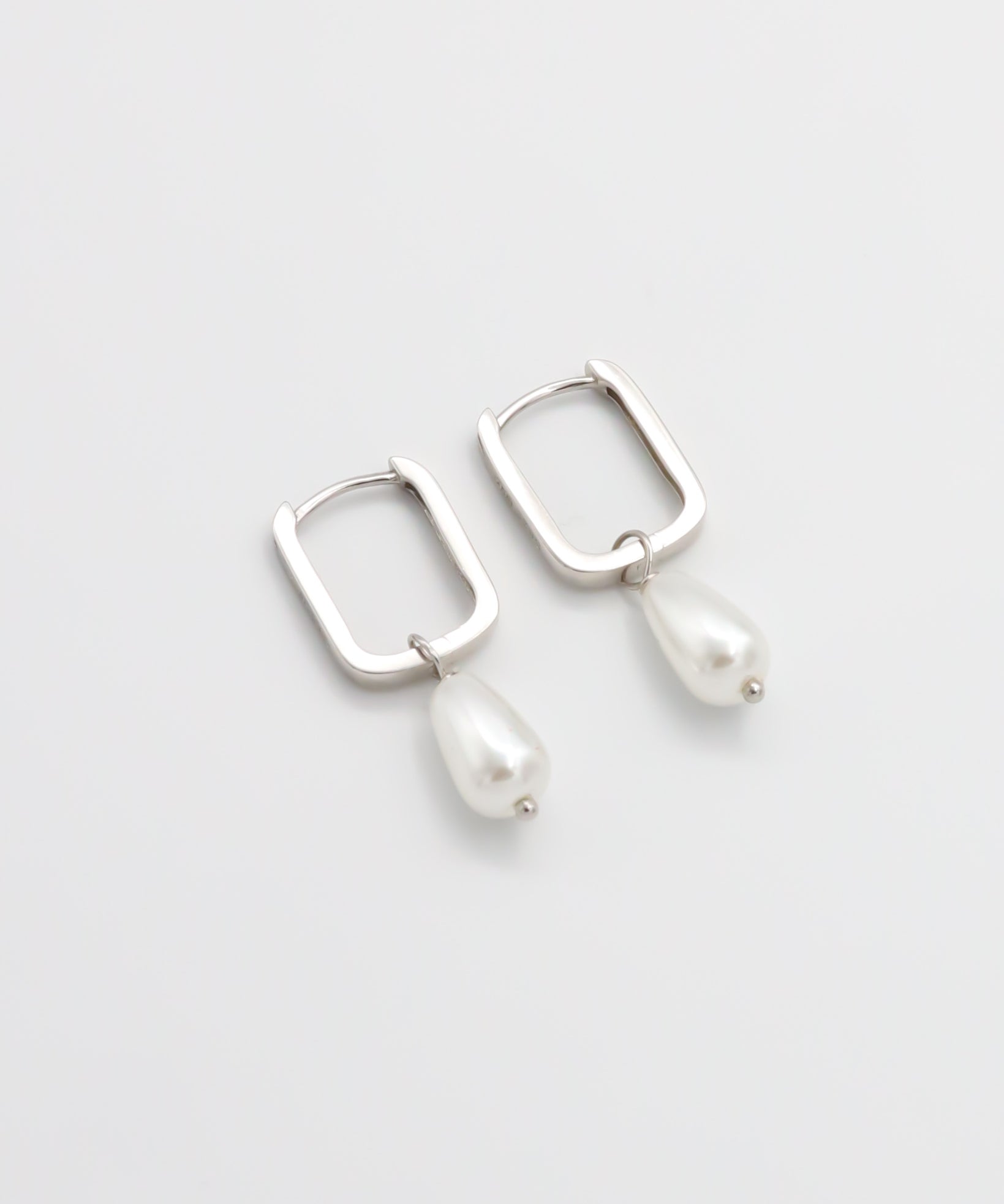 A pair of silver hoop earrings with pearl accents on a white background