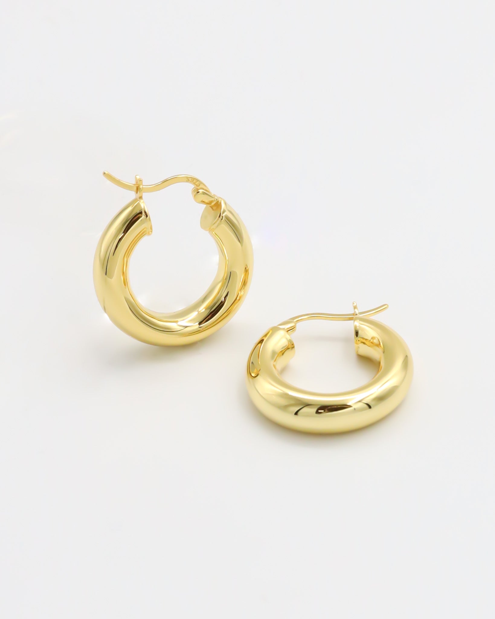 A pair of gold-colored hoop earrings with a latch back closure mechanism, displayed against a white background.