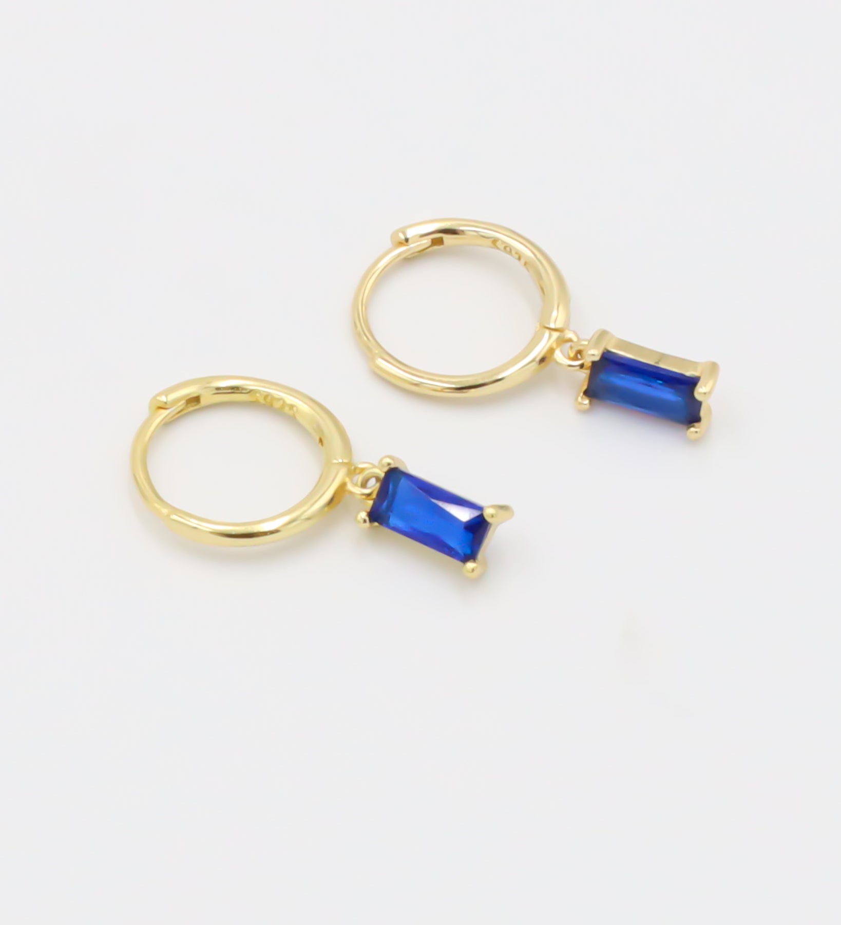 A single gold-colored hoop earring with a blue gemstone attached to it, presented against a white background.