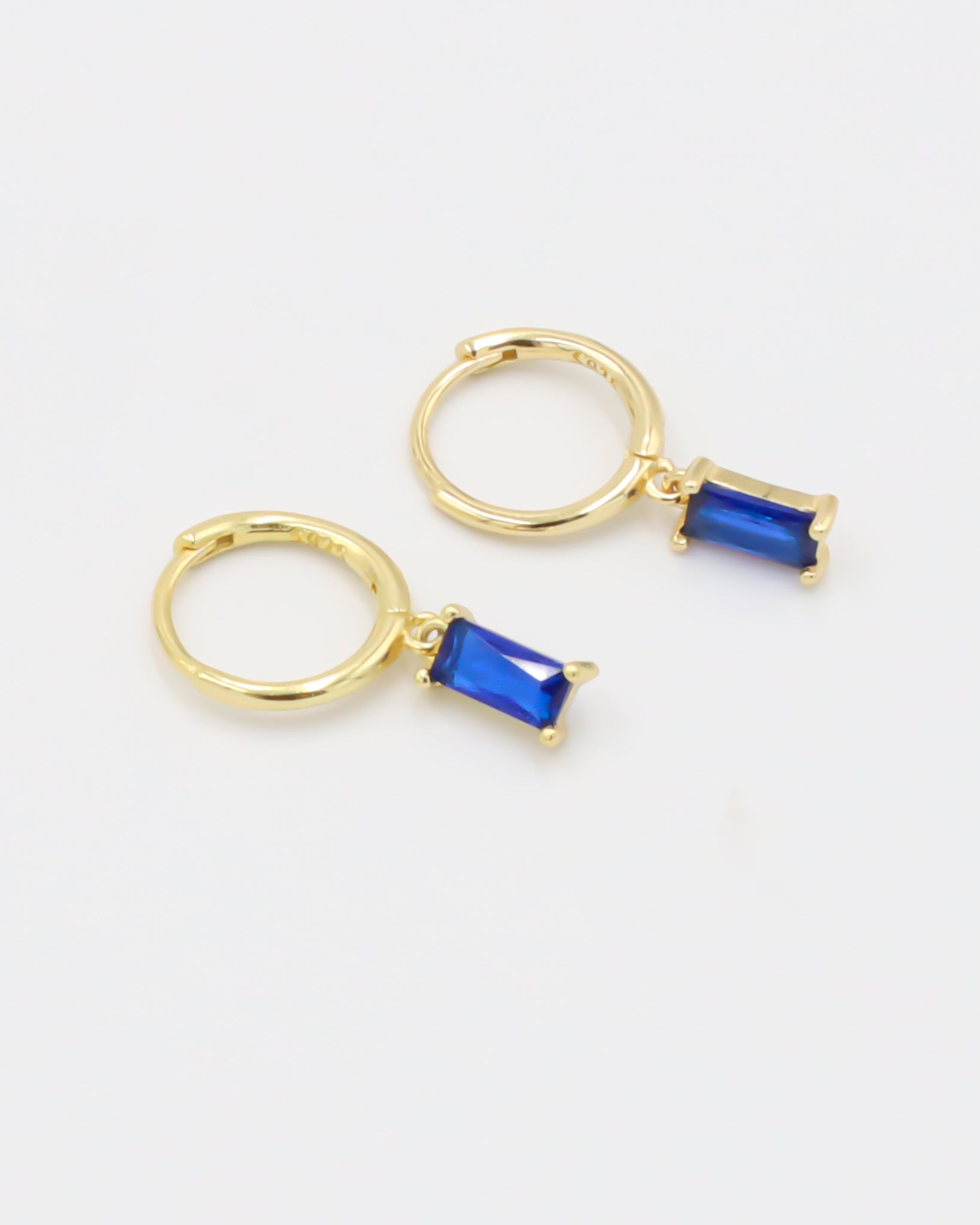 A single gold-colored hoop earring with a blue gemstone attached to it, presented against a white background.