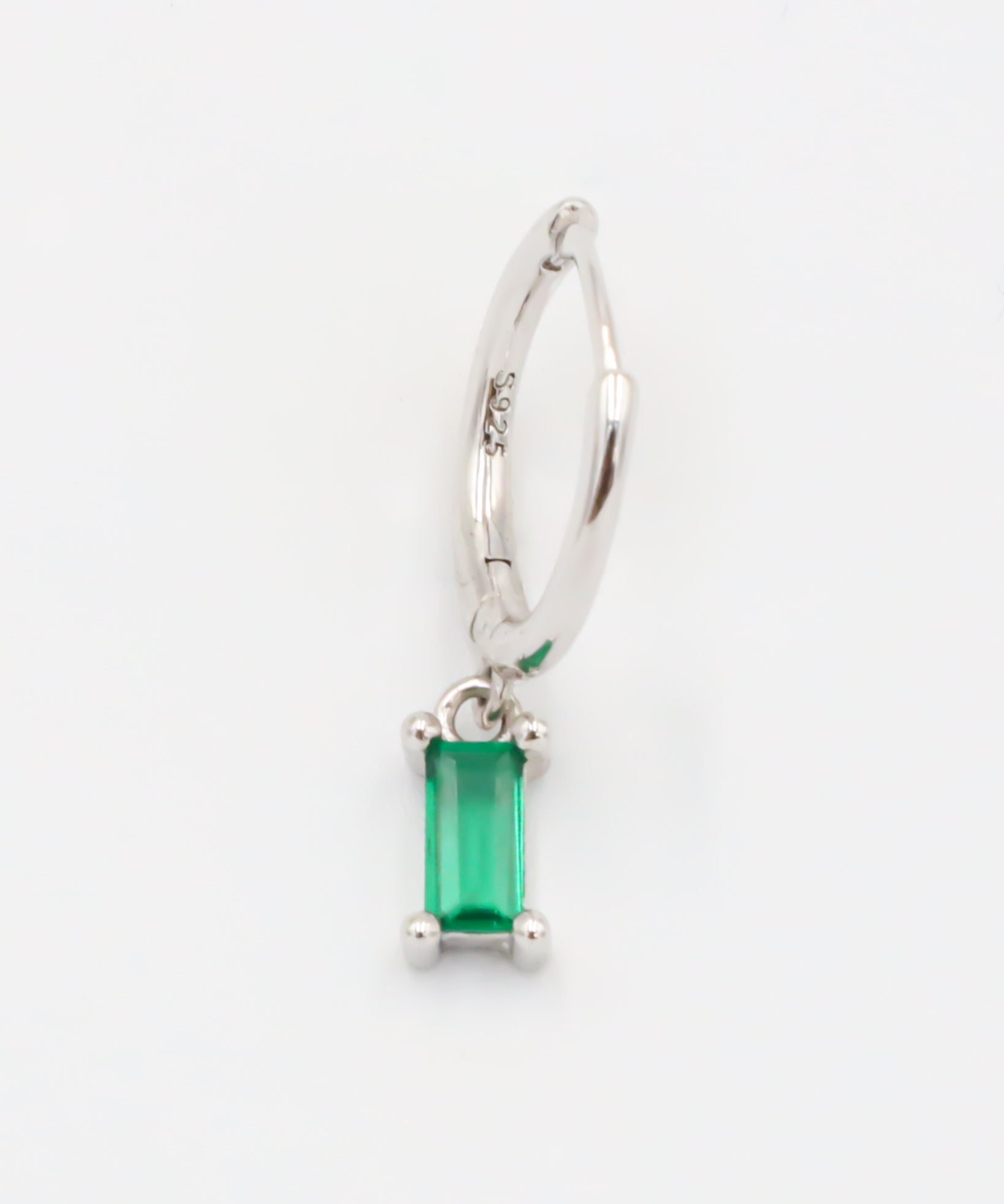 A silver hoop earring with a green gemstone attached to it.