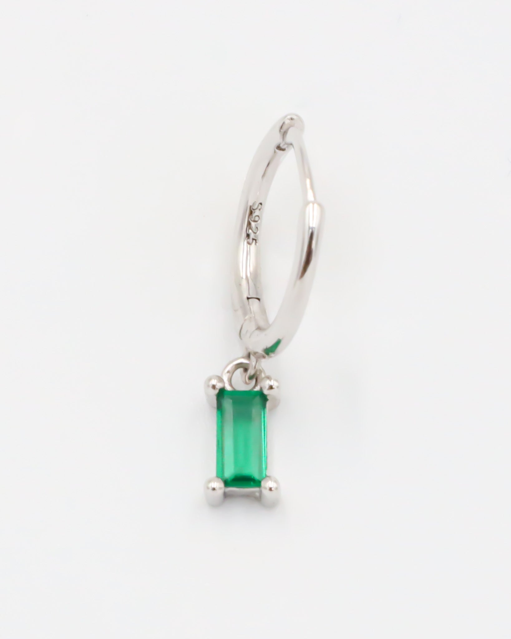 A silver hoop earring with a green gemstone attached to it.