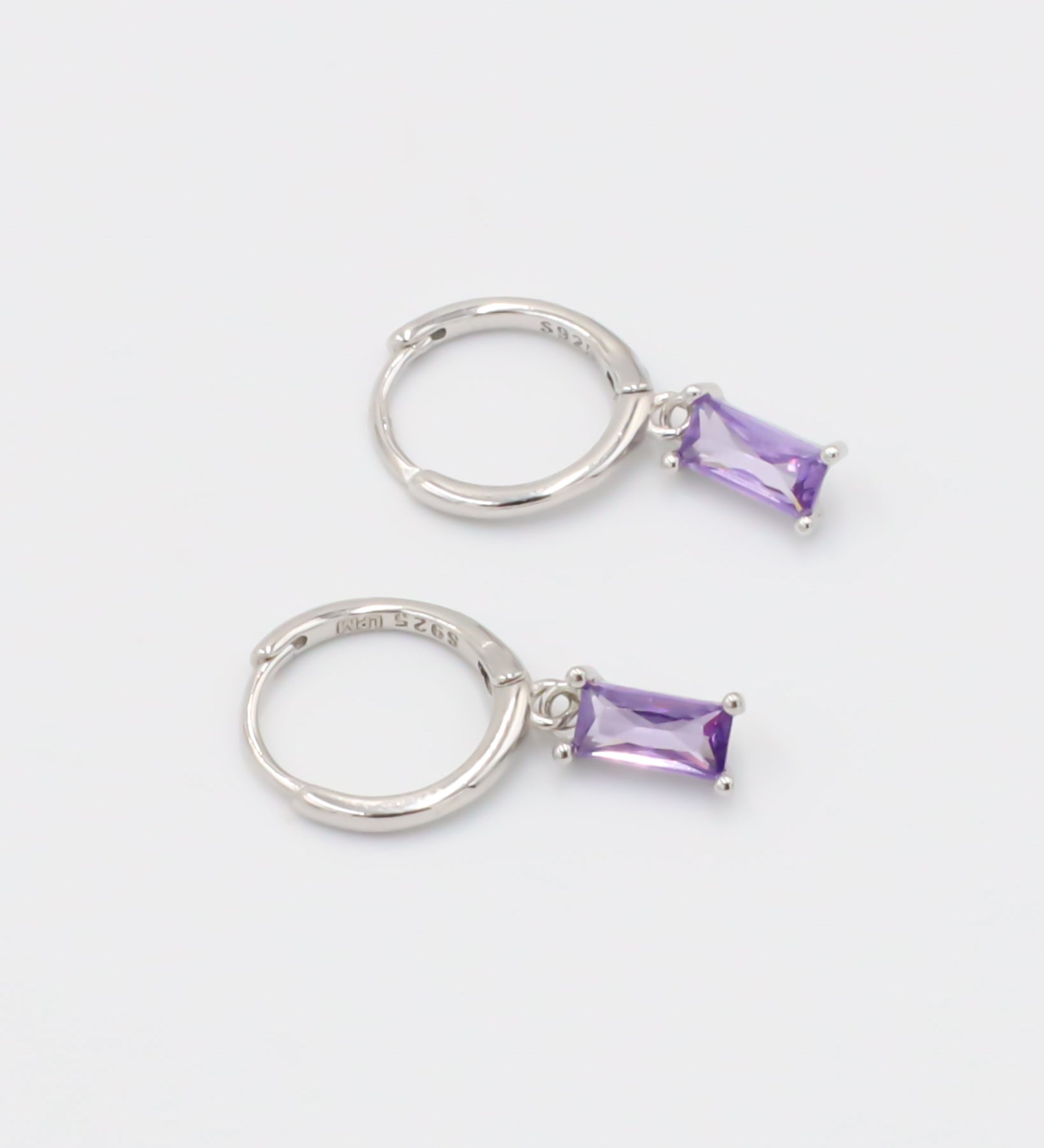 A silver hoop earring with a purple gemstone attached to it, displayed against a white background.