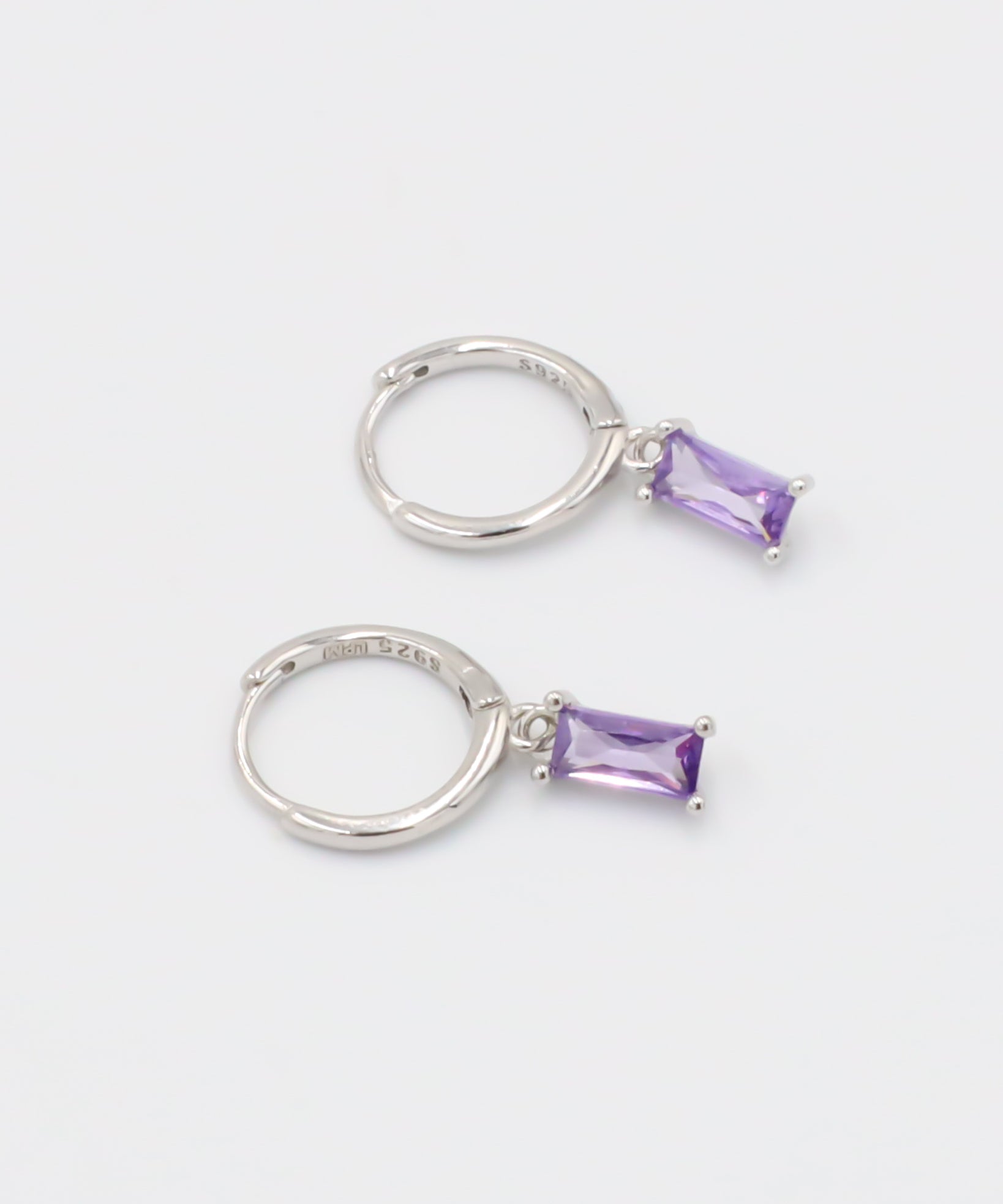 A silver hoop earring with a purple gemstone attached to it, displayed against a white background.