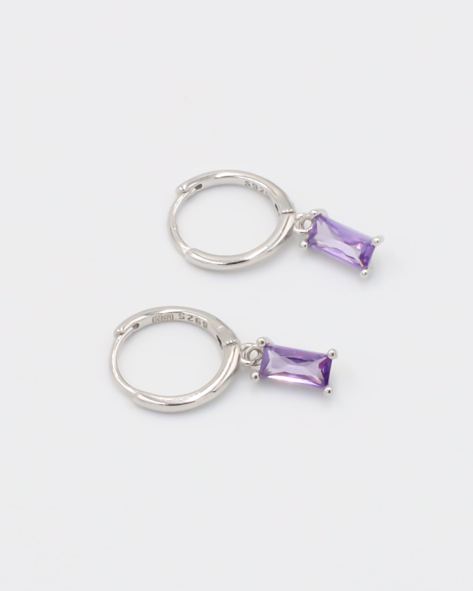 A silver hoop earring with a purple gemstone attached to it, displayed against a white background.