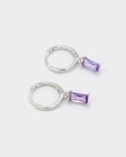 A silver hoop earring with a purple gemstone attached to it, displayed against a white background.