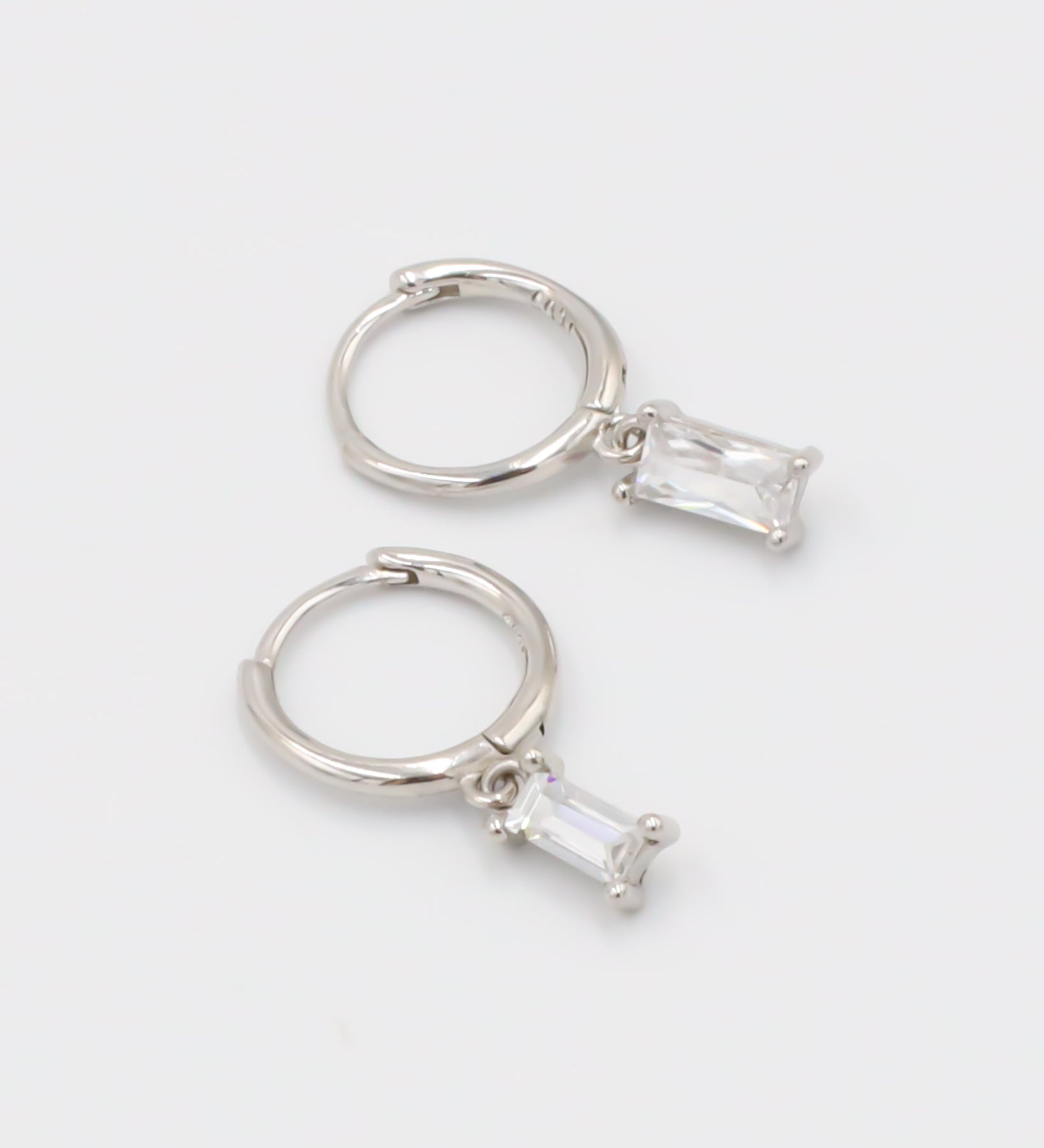 A silver hoop earring with a white stone pendant attached to it, displayed against a white background.