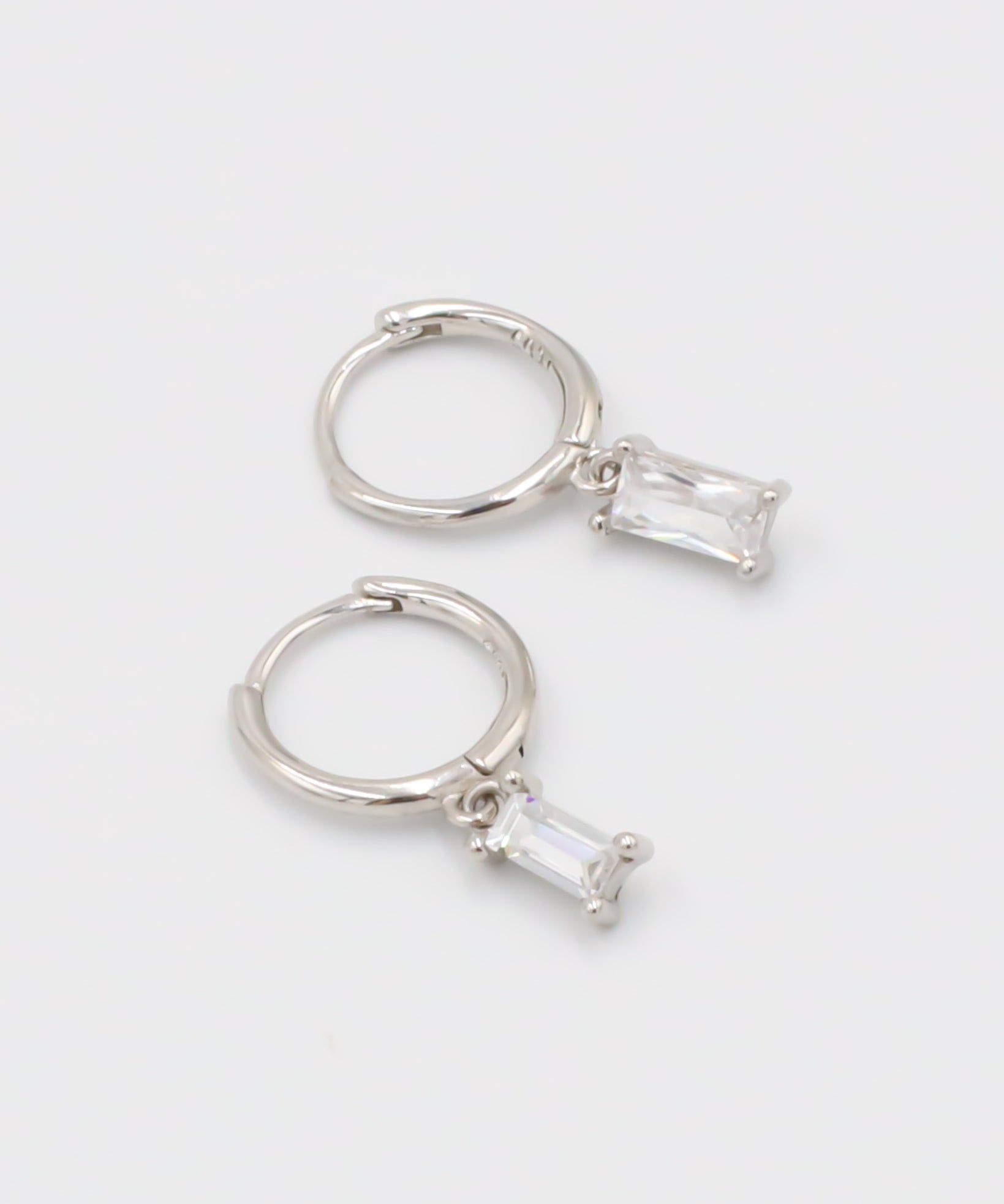 A silver hoop earring with a white stone pendant attached to it, displayed against a white background.