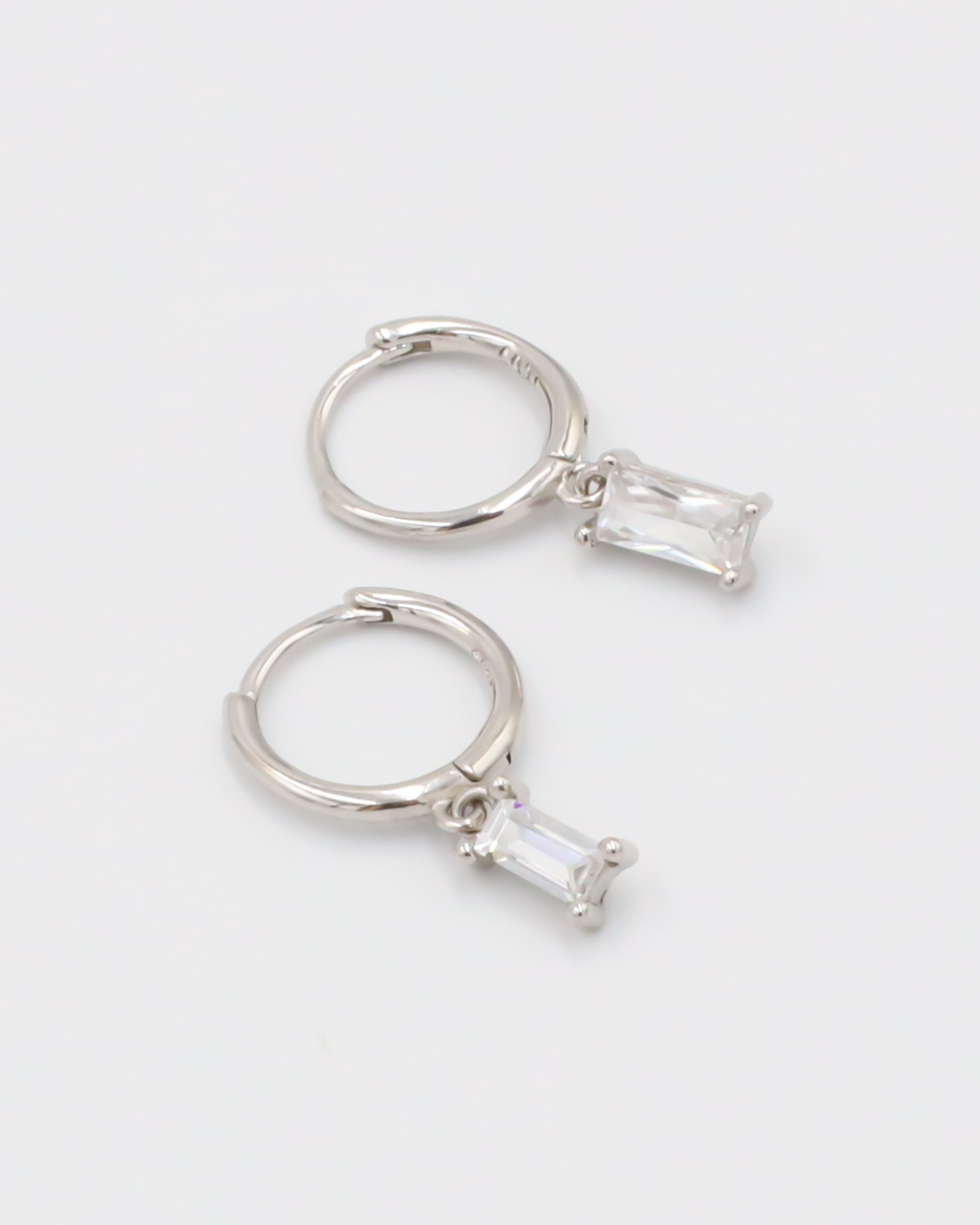 A silver hoop earring with a white stone pendant attached to it, displayed against a white background.