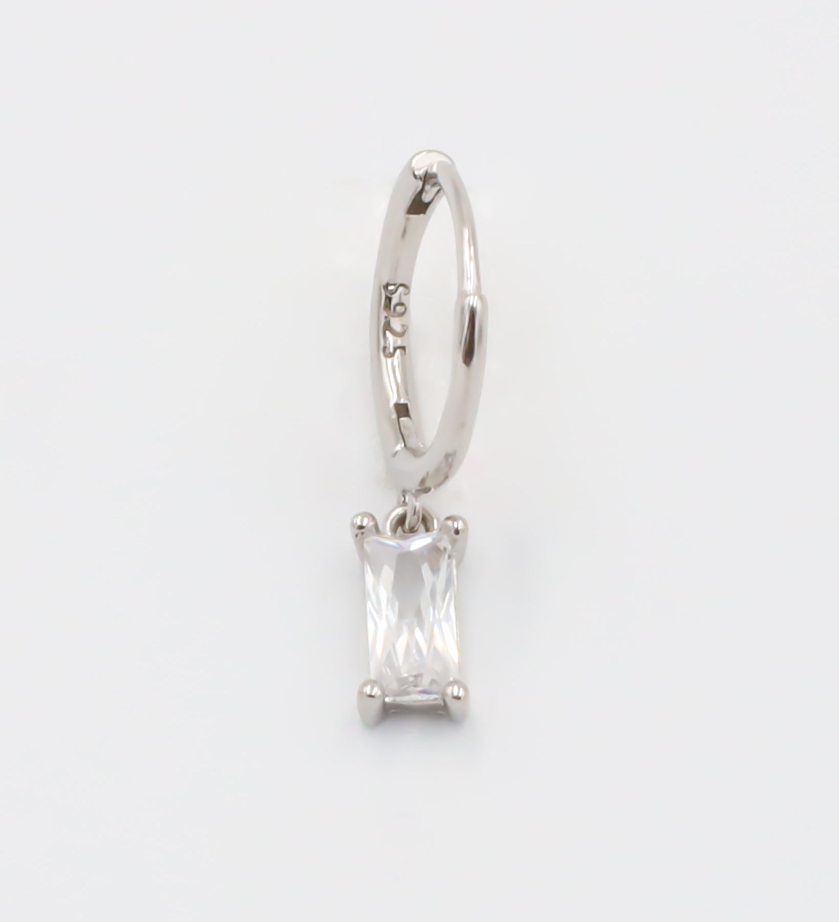 A silver hoop earring with a white stone pendant attached to it, displayed against a white background.