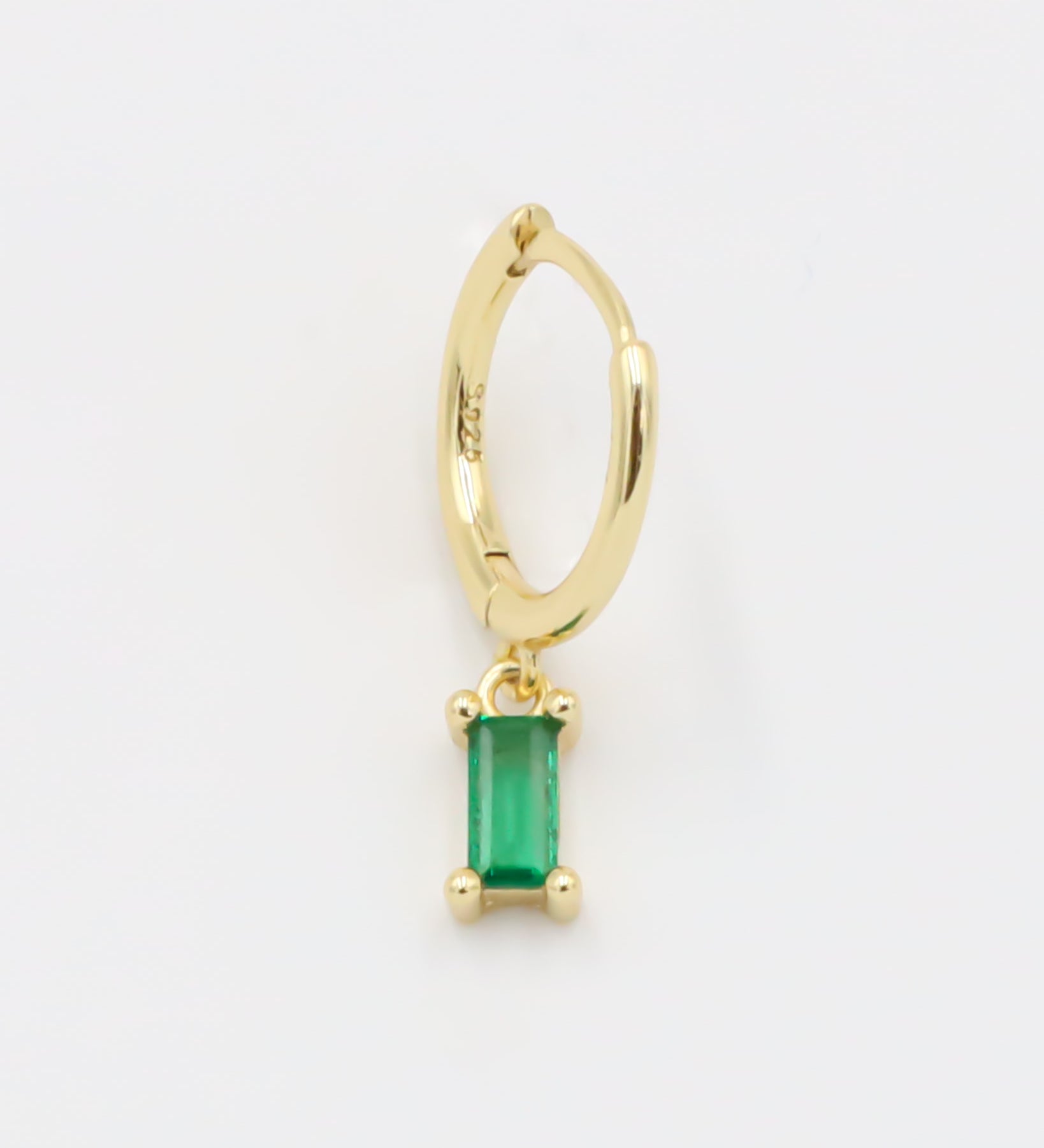 A gold-colored hoop earring with a green square pendant attached to it.