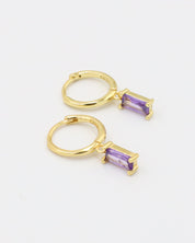 A gold-colored hoop earring with a purple gemstone attached to it, displayed against a white background.