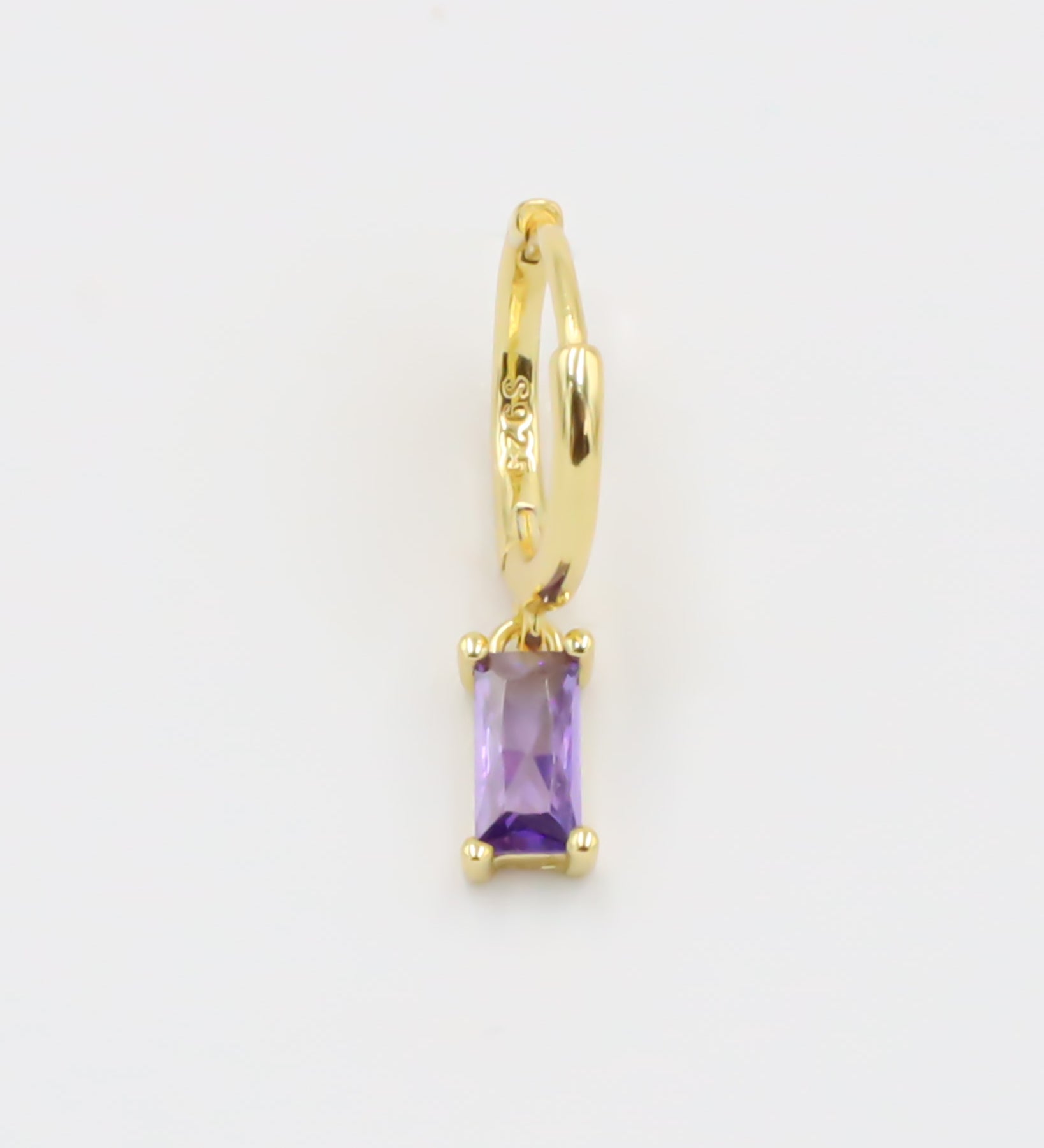 A gold-colored hoop earring with a purple gemstone attached to it, displayed against a white background.