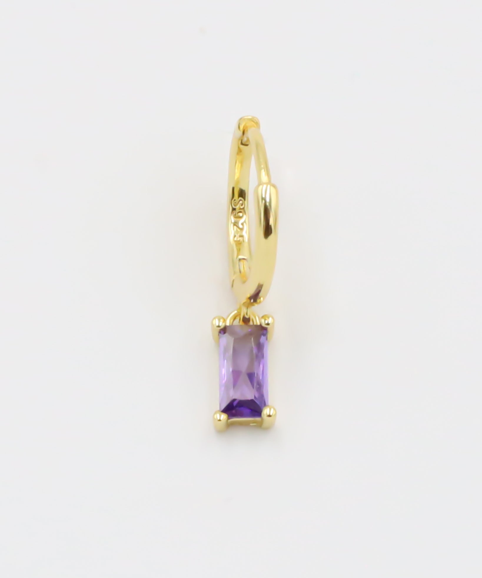A gold-colored hoop earring with a purple gemstone attached to it, displayed against a white background.
