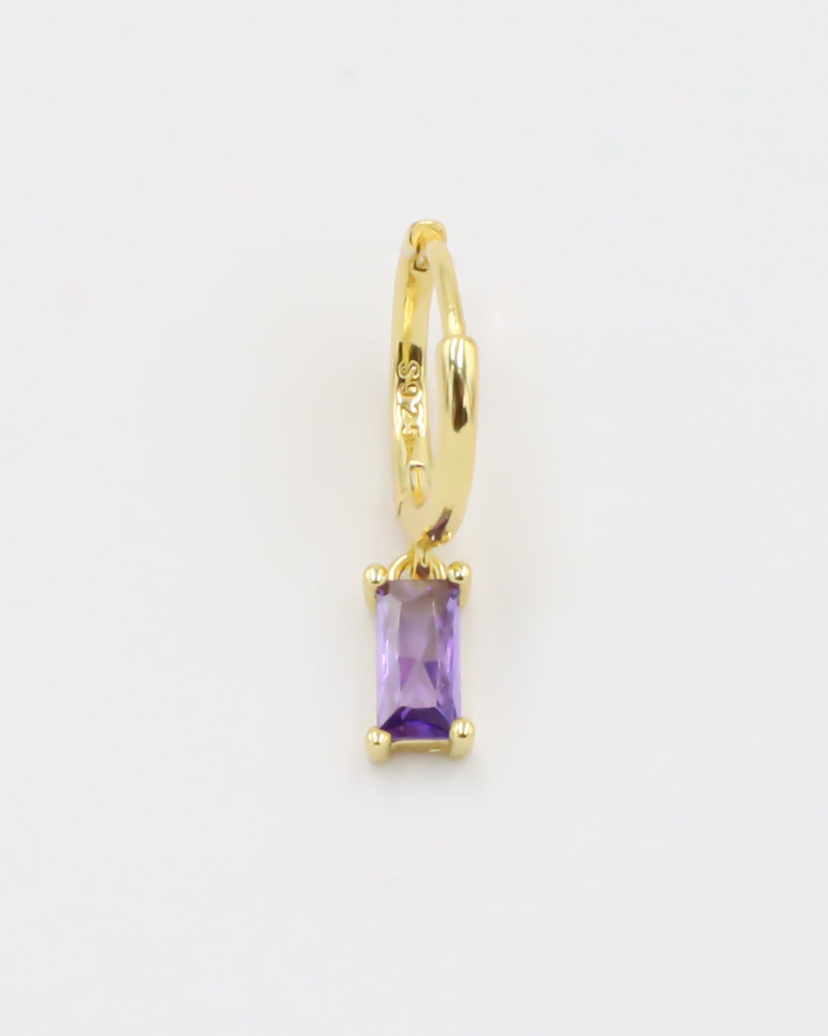 A gold-colored hoop earring with a purple gemstone attached to it, displayed against a white background.