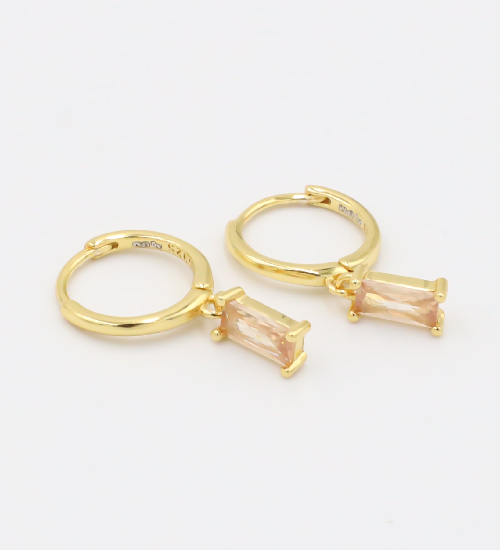 A single gold-colored earring with a peach-colored stone attached to it, presented against a white background.