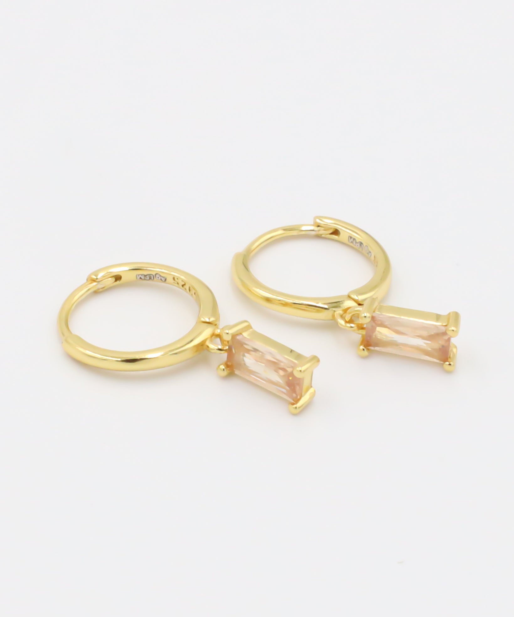 A single gold-colored earring with a peach-colored stone attached to it, presented against a white background.