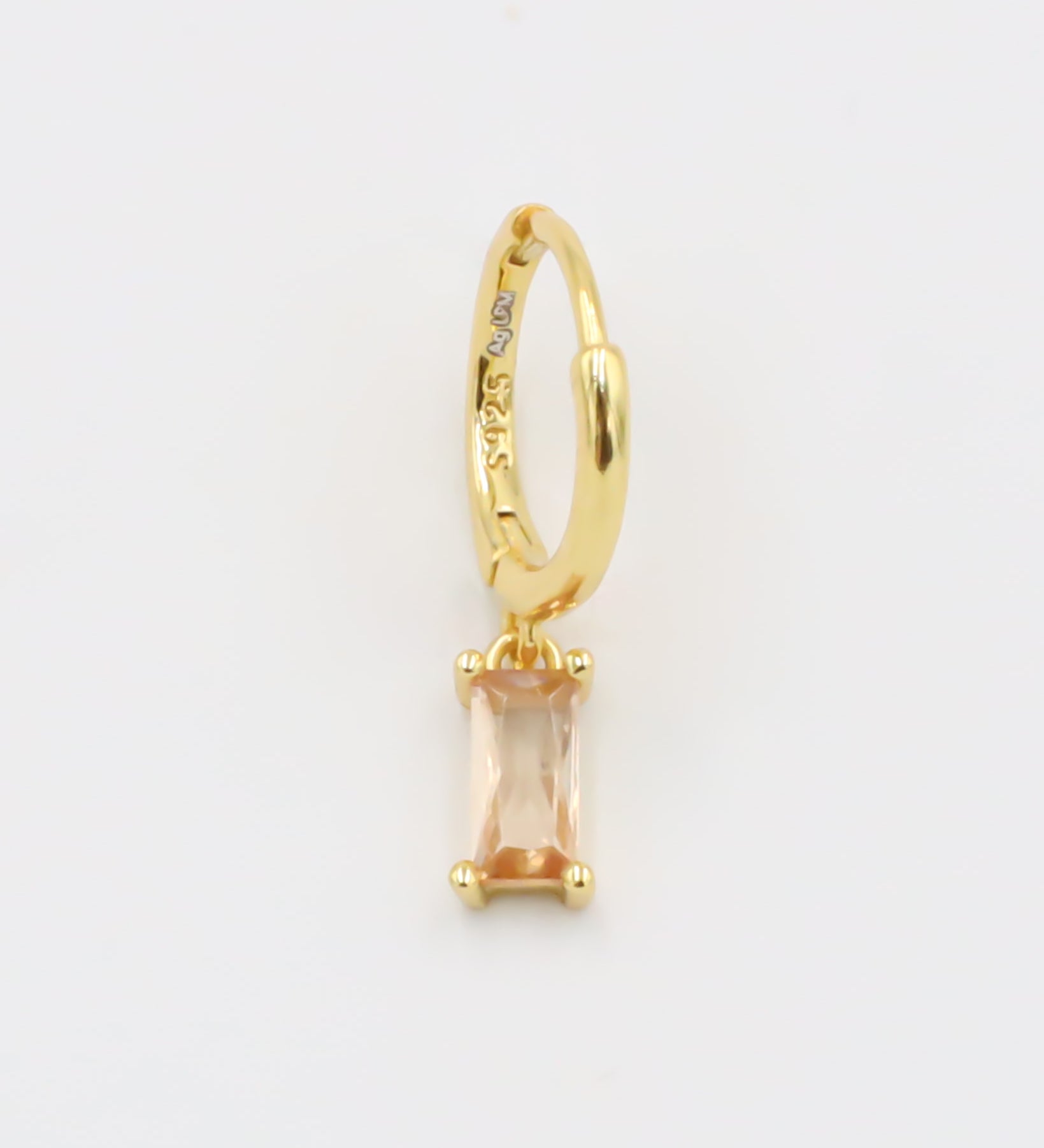 A single gold-colored earring with a peach-colored stone attached to it, presented against a white background.