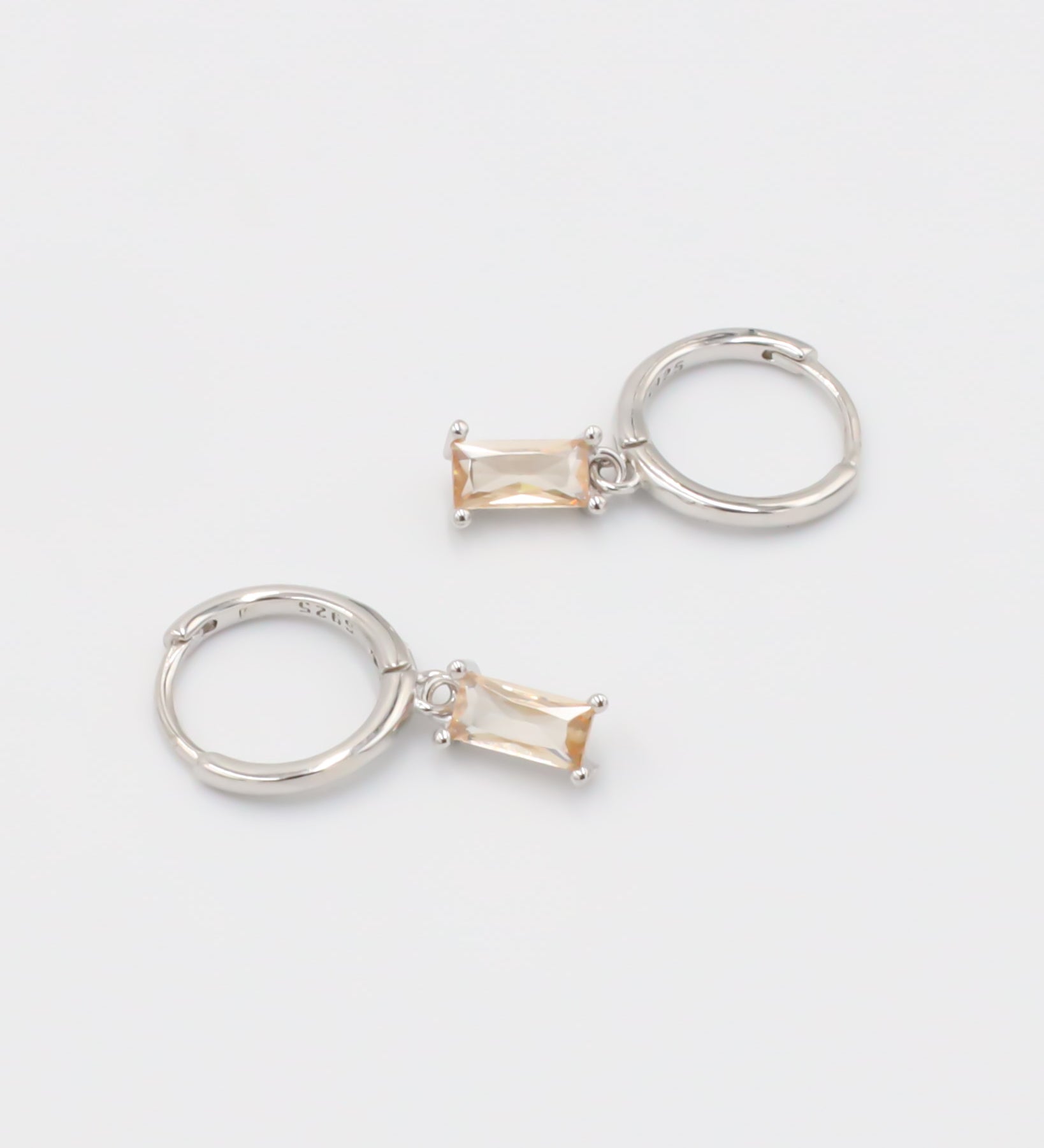 A single silver hoop earring with a peach-colored stone attached to it, displayed against a white background.