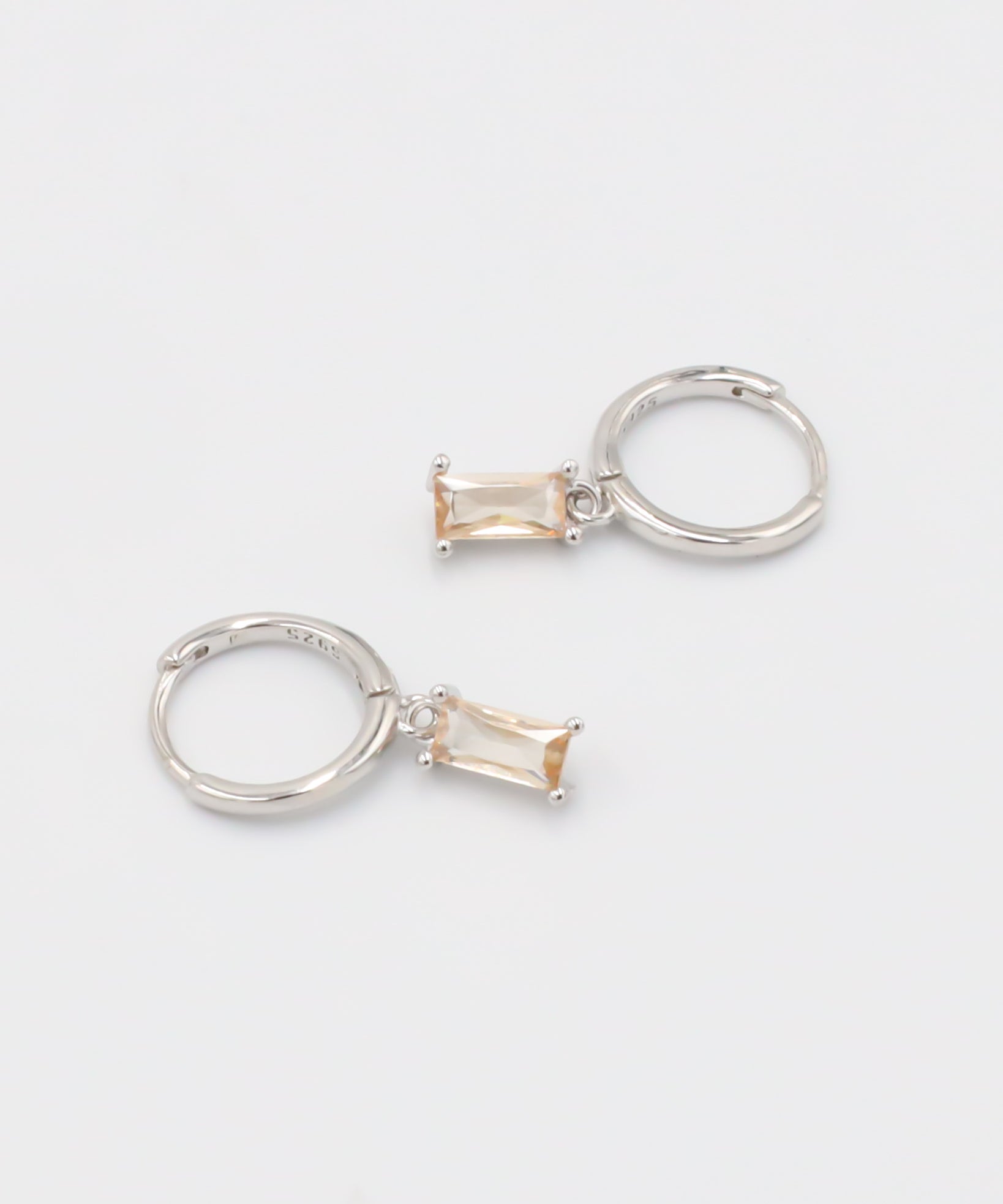 A single silver hoop earring with a peach-colored stone attached to it, displayed against a white background.