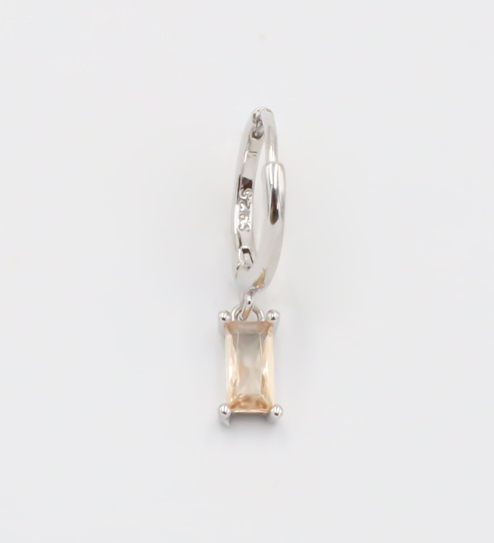 A single silver hoop earring with a peach-colored stone attached to it, displayed against a white background.