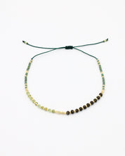 A beaded bracelet with a mix of green, gold, and brown colors, featuring rhinestones and an adjustable cord.