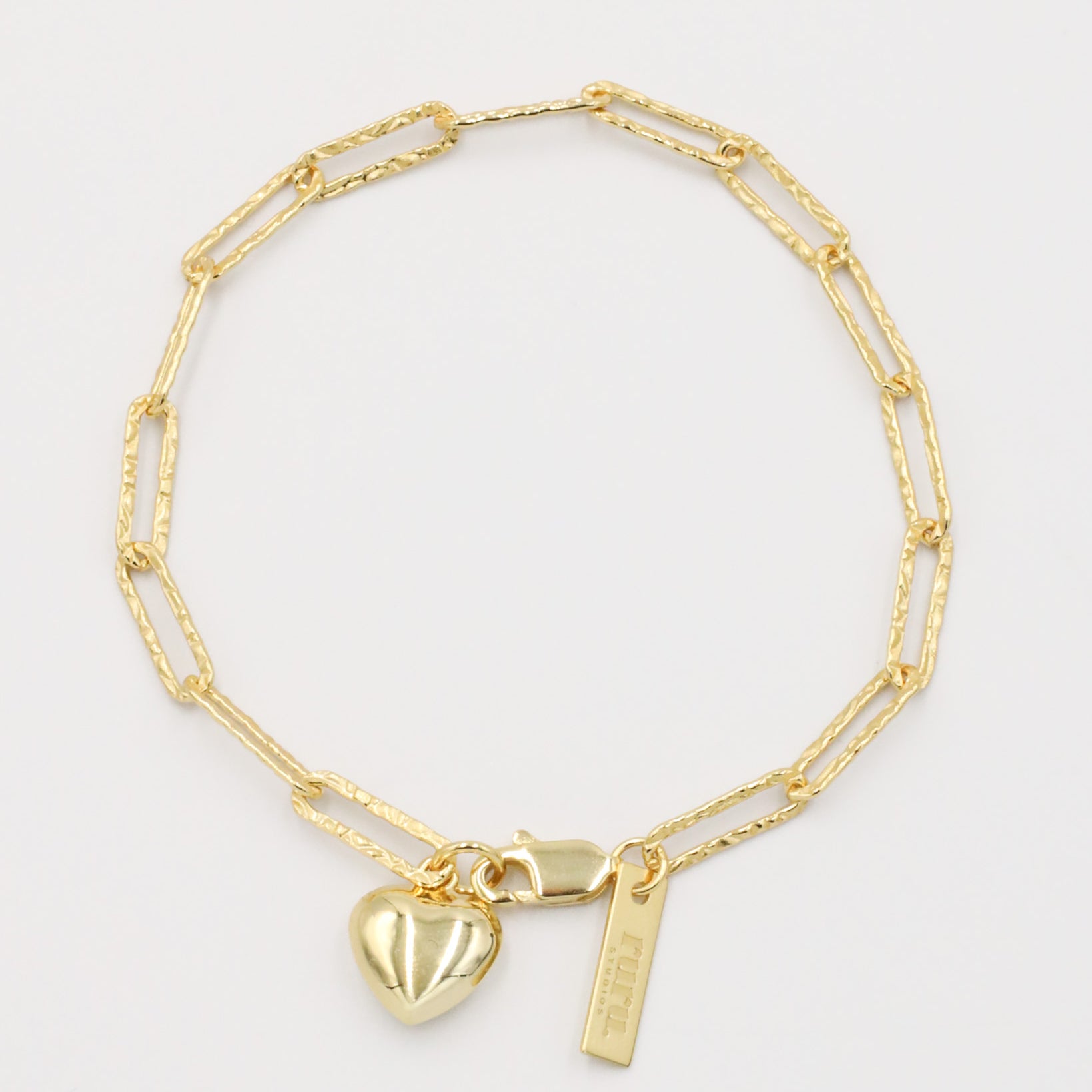 A gold-colored bracelet with a heart-shaped charm and a small tag on a white background.