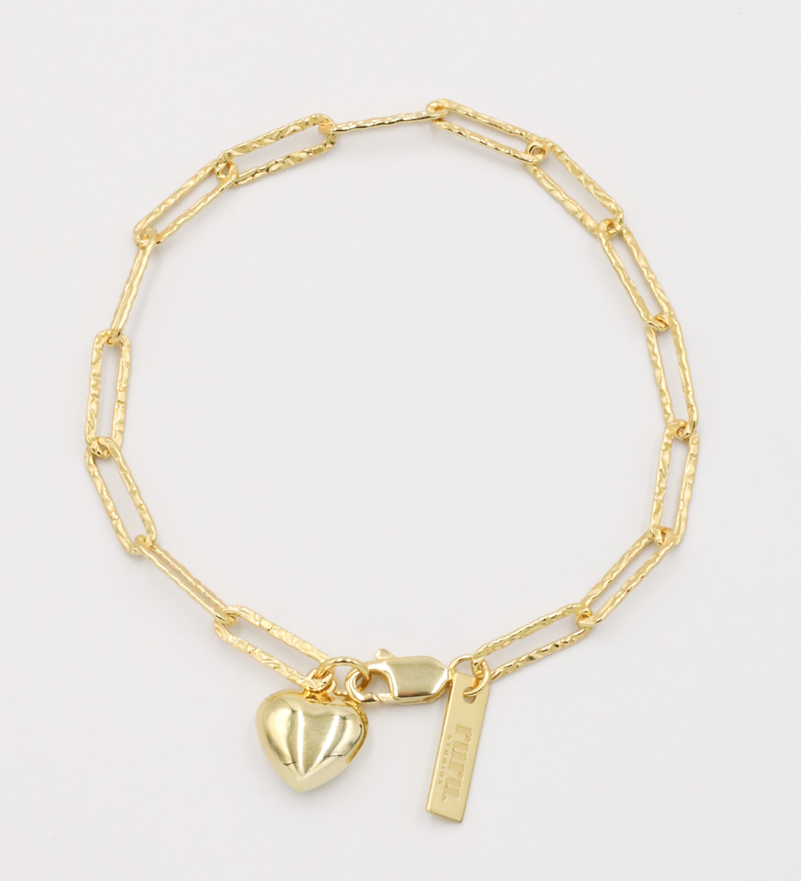 A gold-colored bracelet with a heart-shaped charm and a small tag on a white background.