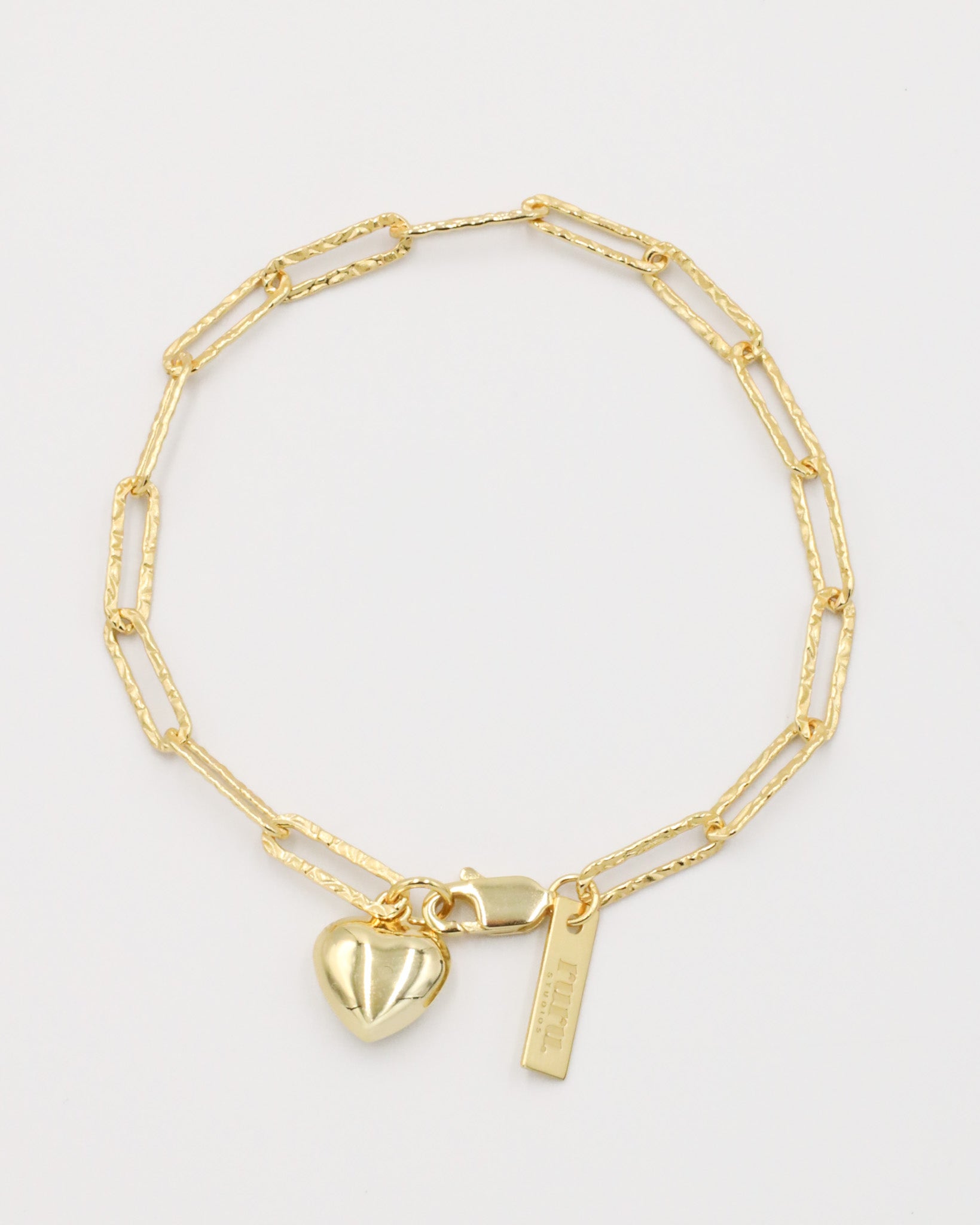 A gold-colored bracelet with a heart-shaped charm and a small tag on a white background.