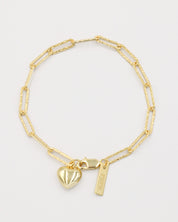 A gold-colored bracelet with a heart-shaped charm and a small tag on a white background.