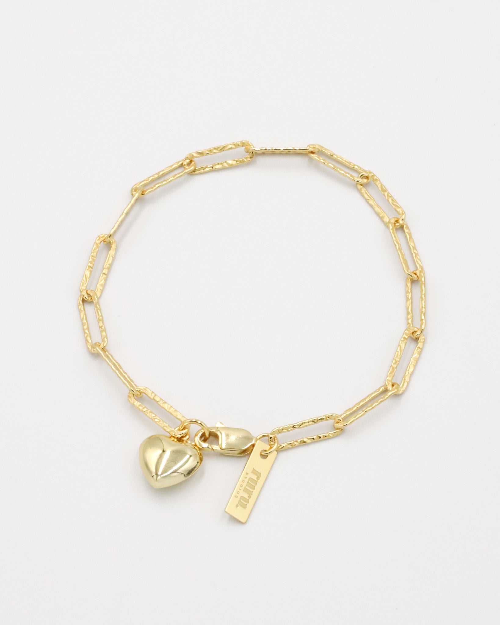A gold-colored bracelet with a heart-shaped charm and a small tag on a white background.