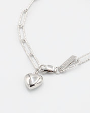 A silver bracelet with a heart-shaped charm on a white background - Close Up.