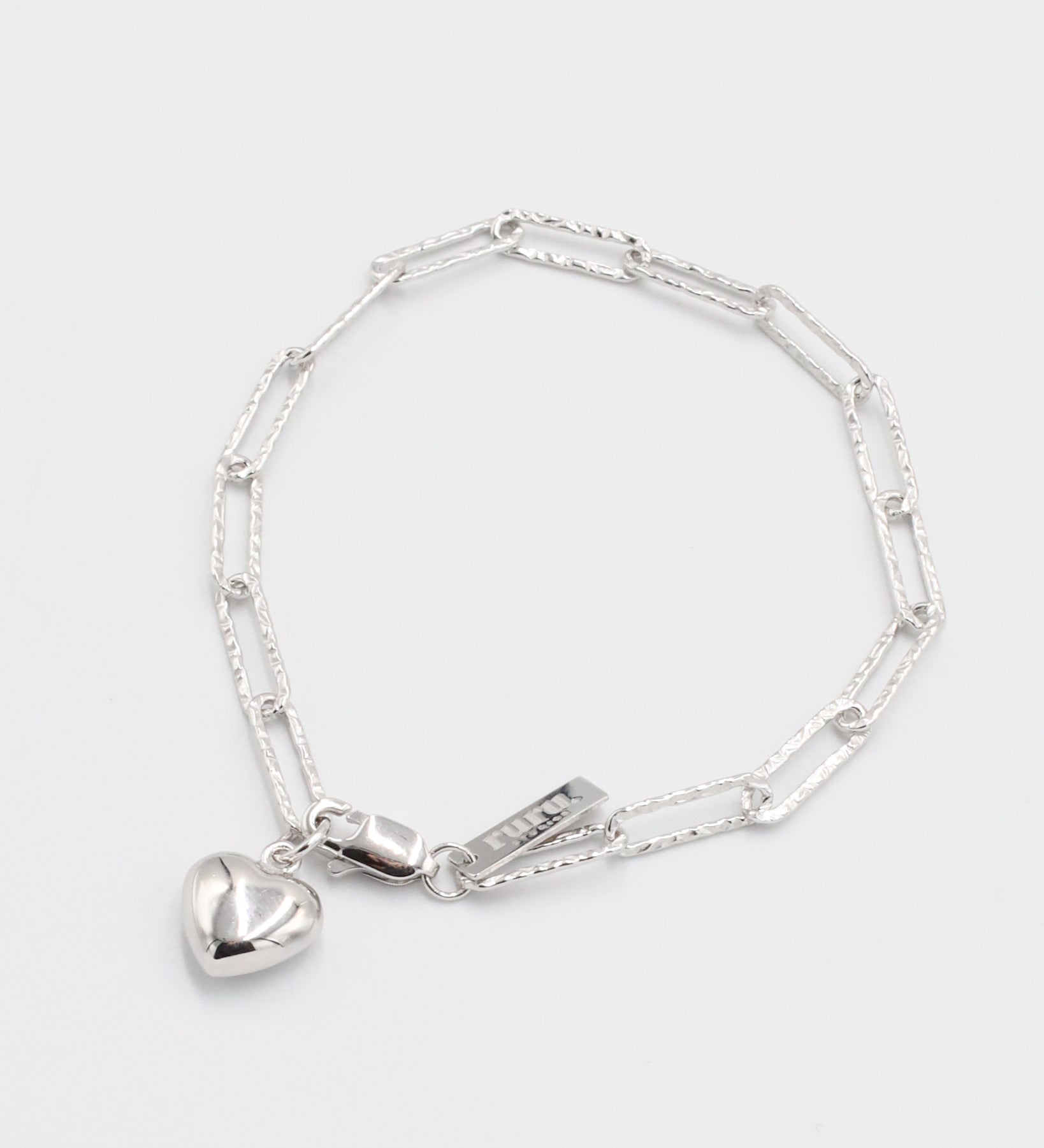 A silver bracelet with a heart-shaped charm on a white background.