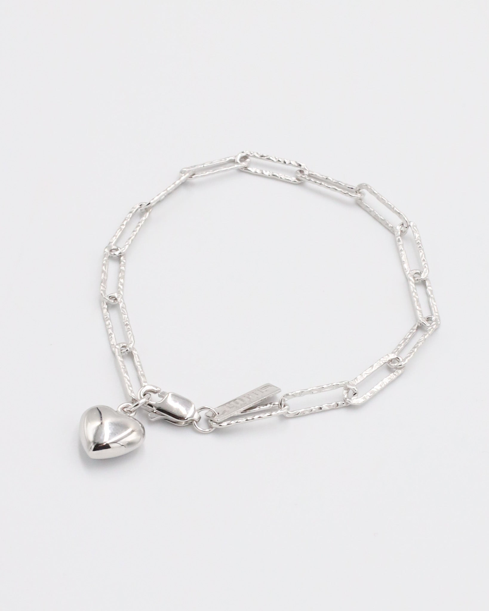 A silver bracelet with a heart-shaped charm on a white background.