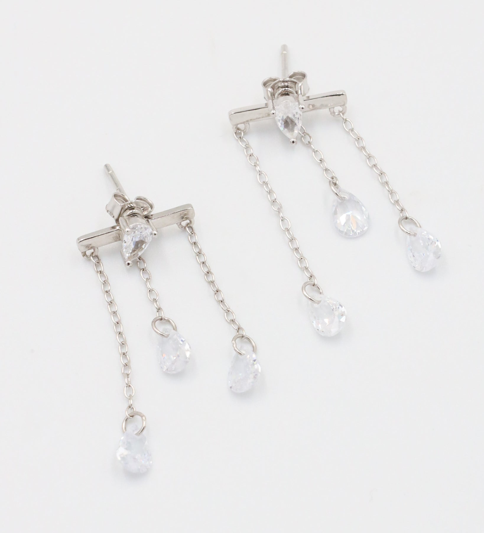 A pair of silver earrings with a stud closure and dangling chain detailed with small clear crystals.