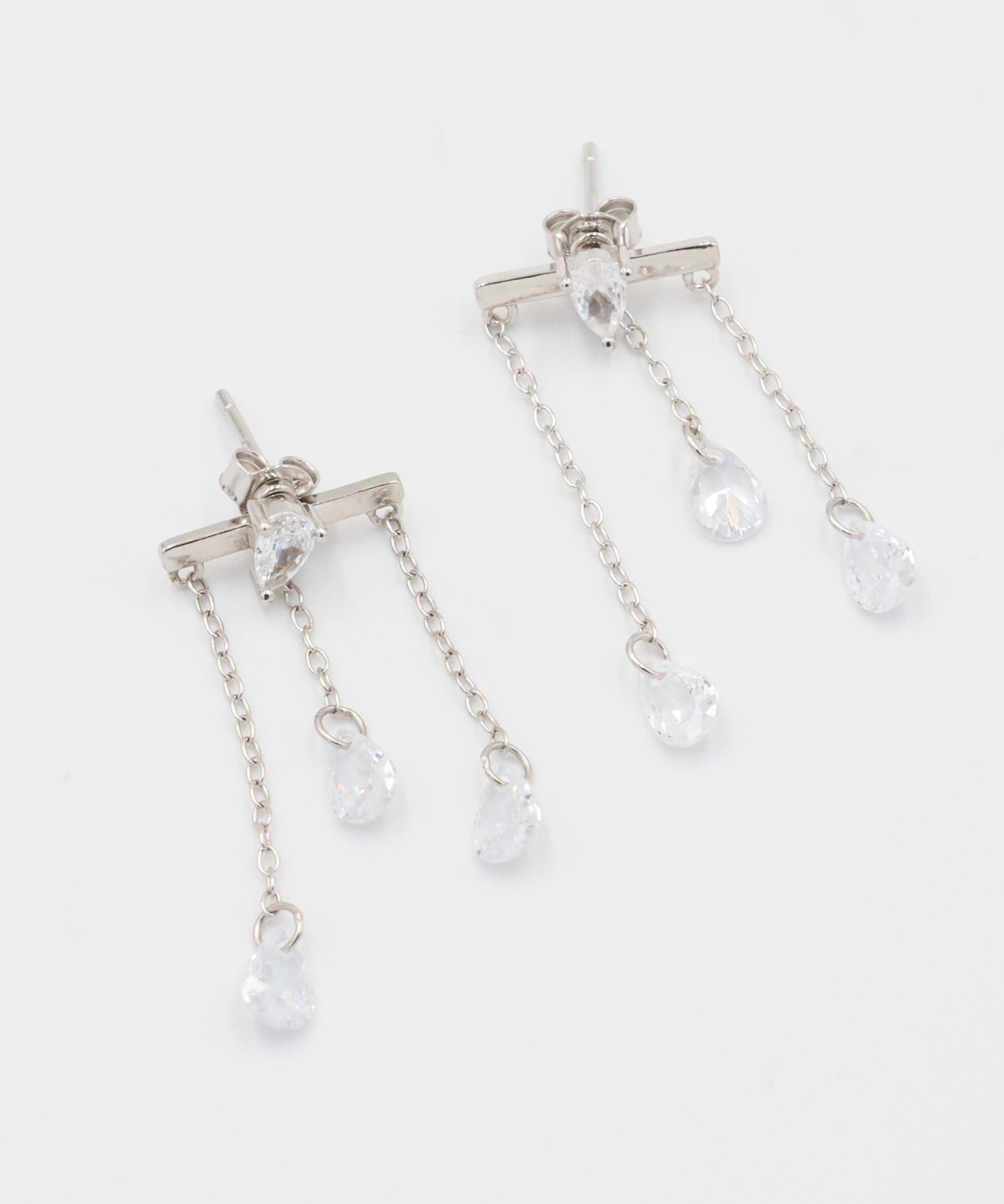 A pair of silver earrings with a stud closure and dangling chain detailed with small clear crystals.
