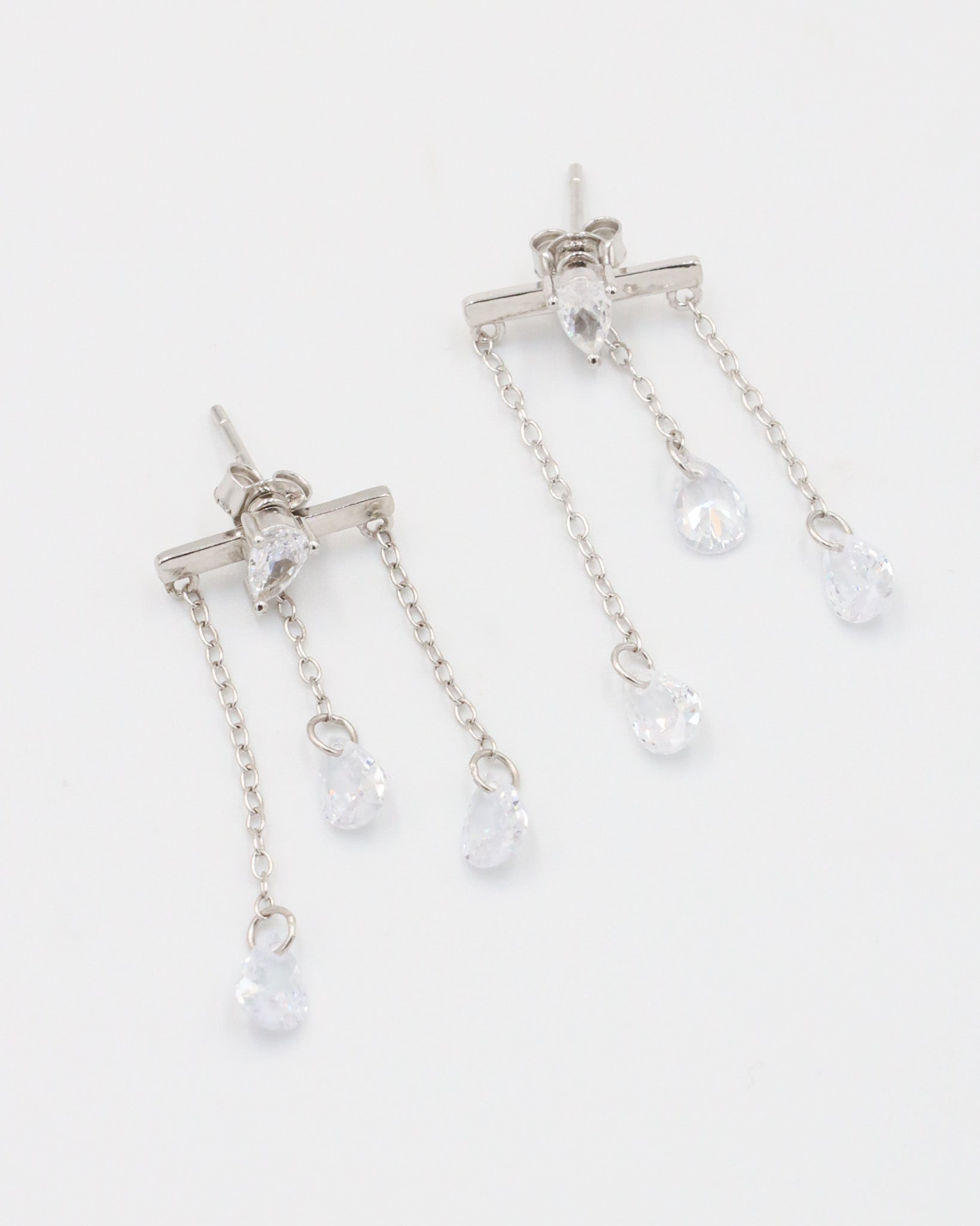 A pair of silver earrings with a stud closure and dangling chain detailed with small clear crystals.