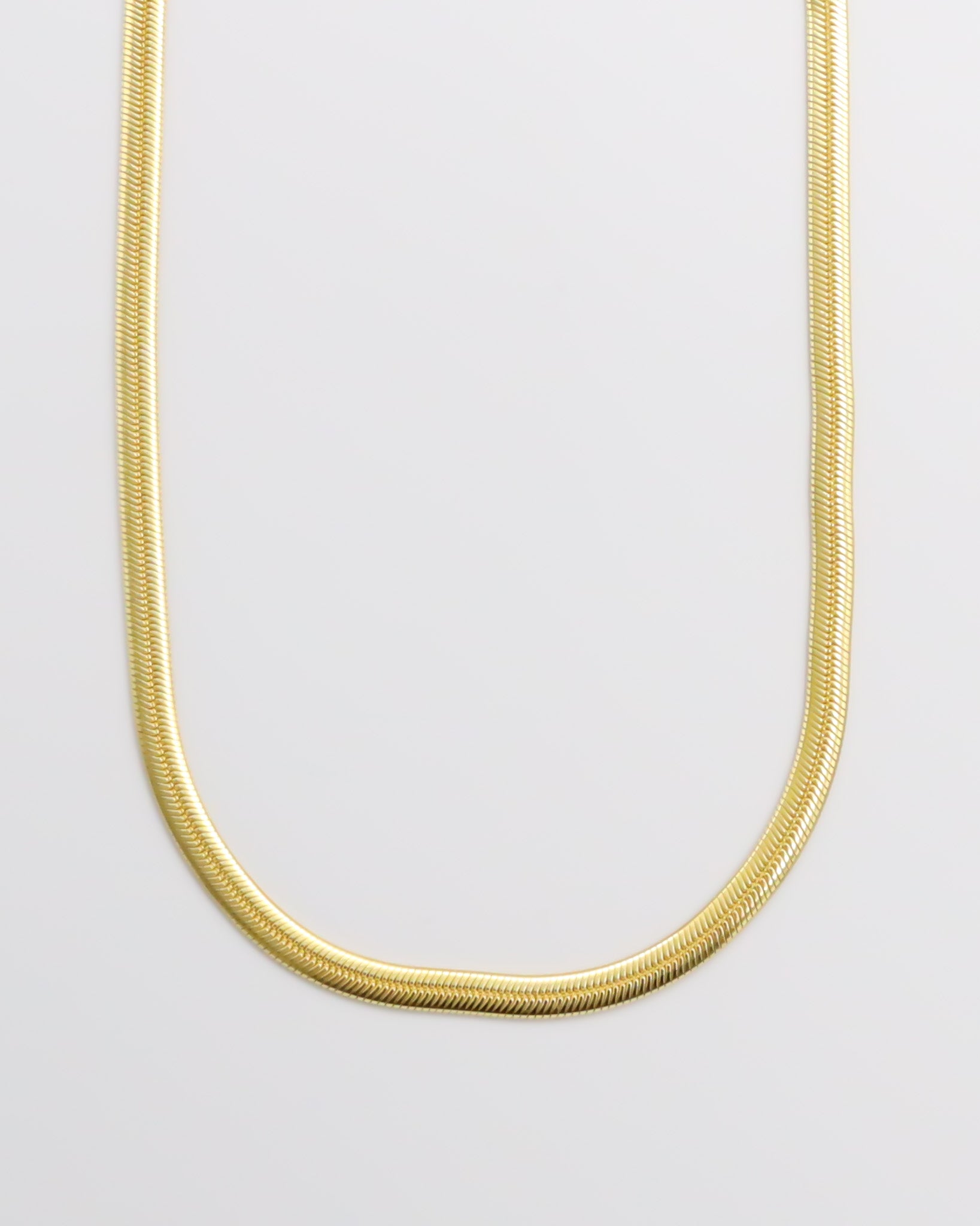 A gold-colored necklace laid out on a plain surface.