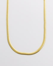 A gold-colored necklace laid out on a plain surface.