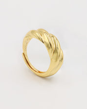 A gold-colored ring with a twisted design standing on a white background