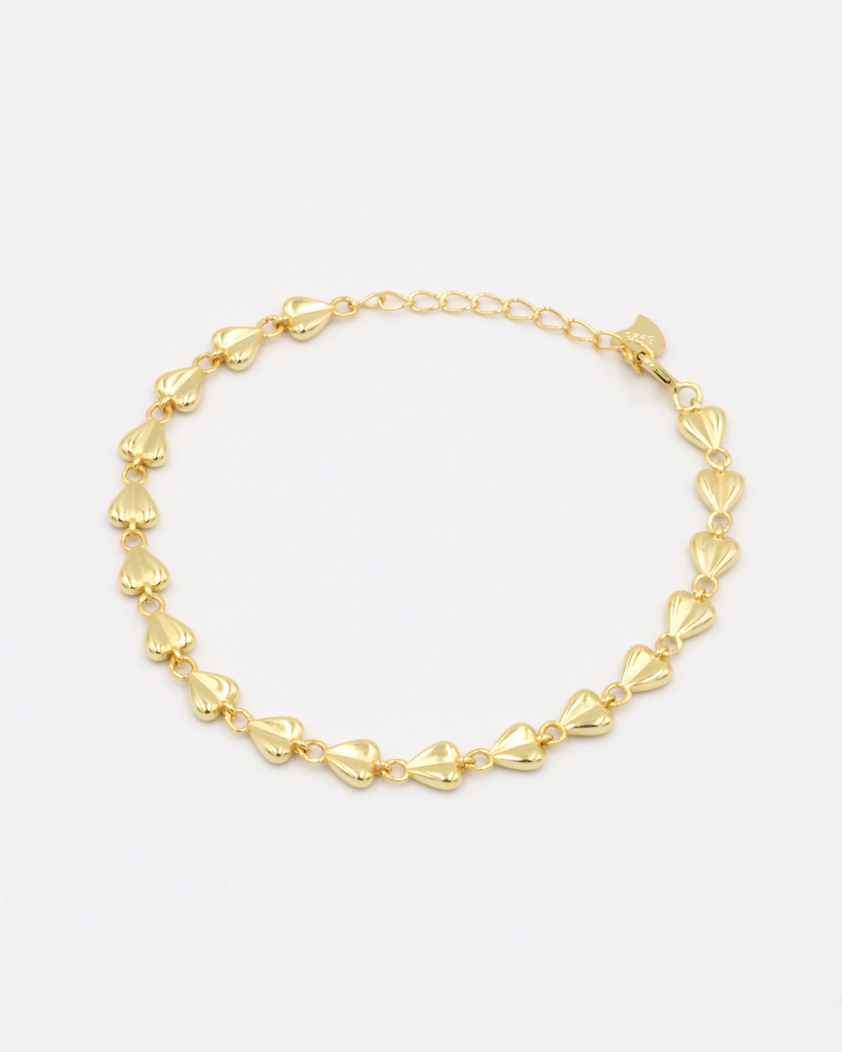 A gold bracelet with a heart-shaped pattern on a white background