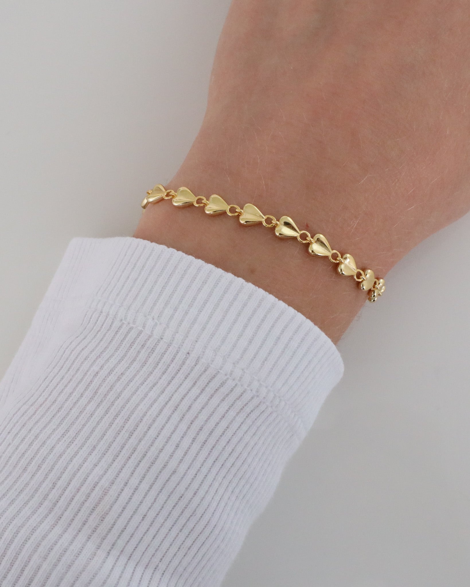 Close-up of a wrist wearing the delicate Josie bracelet with heart-shaped elements and a polished finish, styled with a white ribbed long sleeve.