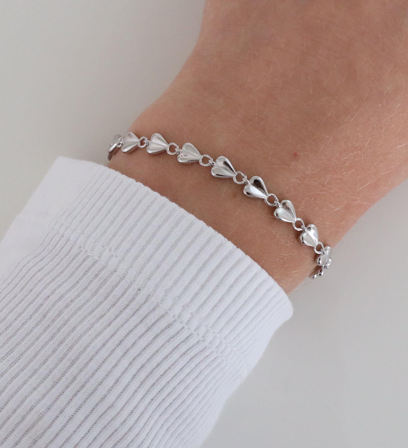 Close-up of a wrist wearing the delicate Josie bracelet with heart-shaped elements and a polished finish, styled with a white ribbed long sleeve.